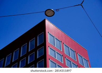 Modern red building featuring multiple windows and a single street lamp against a clear blue sky