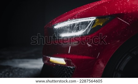 Modern Red Performance Vehicle with LED Headlights is Being Cleaned at a Dealership Car Wash. Close Up Commercial Photo of a Fast Car Being Washed in a Low Key Cinematic Studio