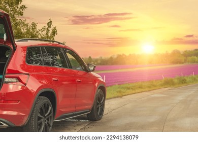 Modern red SUV car parked on rural road near blooming flower field against scenic warm evening sunset light sky landscape. Family countryside vacation auto journey trip at nature outdoors - Powered by Shutterstock