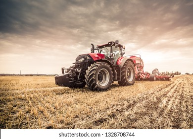 Modern red tractor seeding directly into the stubble with red equipment using GPS for precision farming in the fields of Czech Republic.