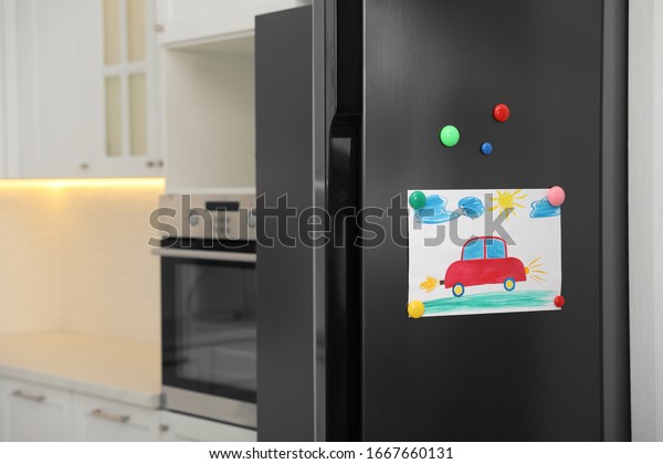 Modern refrigerator with child\'s drawing and\
magnets in kitchen