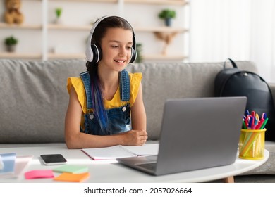 Modern Remote Learning Concept. Happy teen girl in headset studying online, sitting on sofa at desk, using laptop looking at screen, watching webinar, participating in lesson listening to teacher - Shutterstock ID 2057026664