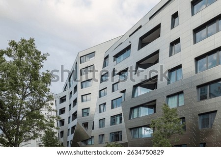A modern residential building featuring an angular, irregular facade clad in metallic panels. 
