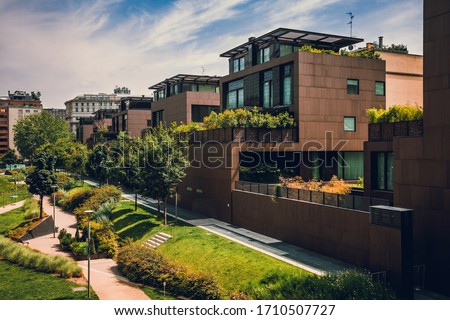 Modern residential buildings in the public green area. Apartment houses in Europe. Beautiful view of real estate homes in Milan, Italy. Business district in summer. Walking area with trees and grass.
