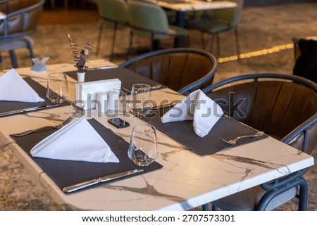 A modern restaurant table set for dining. The table features a marble top with neatly folded napkins and glassware. Stylish chairs surround the table