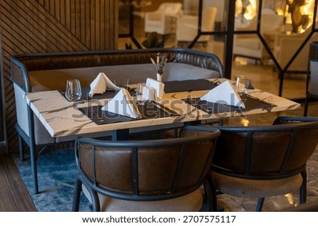 A modern restaurant table set for dining. The table features a marble top with neatly folded napkins and glassware. Stylish chairs surround the table