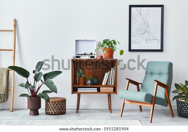 Modern retro composition of living room
interior with design wooden cabinet, stylish armchair, mock up
poster map, plants, vinyl recorder, books and personal accessories
in home decor. Template.
