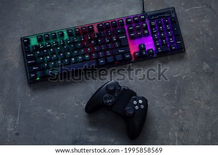Modern RGB keyboard and game pad on grey table, flat lay