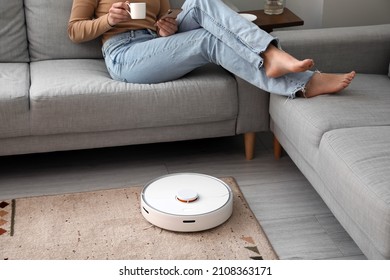 Moderna aspiradora robot cerca del sofá con mujer en reposo en la habitación