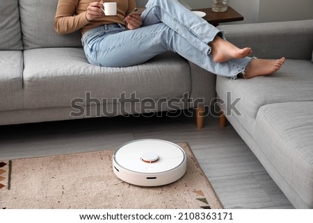 Modern robot vacuum cleaner near sofa with resting woman in room Сток-фото © 