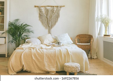 Modern Romantic Scandi Boho Style Bedroom Interior With Decorative Pillows, Green Plant And Diy Macrame Wall Panel. Light Warm Cozy Comfortable Home. Jomo, Weekend Breakfast In Bed Concept.