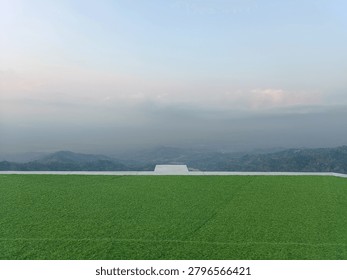Modern rooftop viewing deck with artificial green grass lawn overlooking a misty mountain landscape.