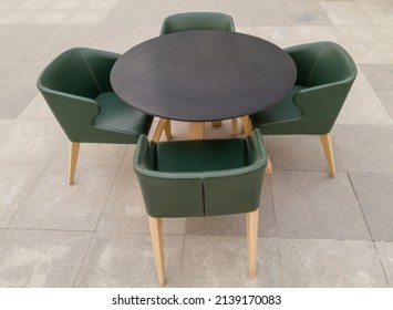 Modern round black dining table with four green leather armchairs on a paved outdoor patio