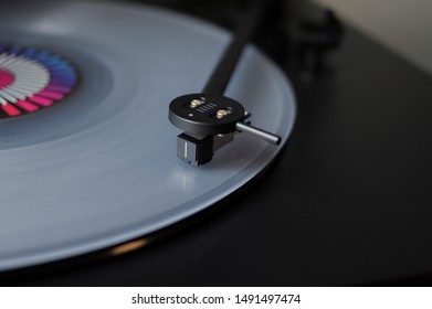 Modern round headshell with black cartridge on straight tonearm and transparent clear white vinyl record disc spinning on belt drive turntable - Shutterstock ID 1491497474