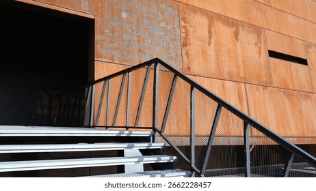 A modern rust-colored building with sharp geometric lines stands out against a clear blue sky