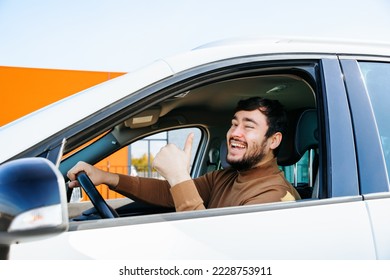 modern satisfied chauffeur bearded young man sitting in a car shows thumb up from window. Man smiles, mouth wide open. Portrait of happy man showing ok sign - Shutterstock ID 2228753911