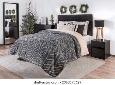 Modern Scandinavian Bedroom Interior with a Padded Fabric Headboard, Warm Black Cover, and Striped cozy Pillows on the Bed, beside a Wooden Nightstand Featuring Christmas Decorations. - Powered by Shutterstock