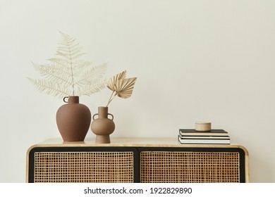 Modern scandinavian home interior with design wooden commode, dried leafs in ceramic vases and personal accessories in stylish home decor. Template. Copy space. White walls.