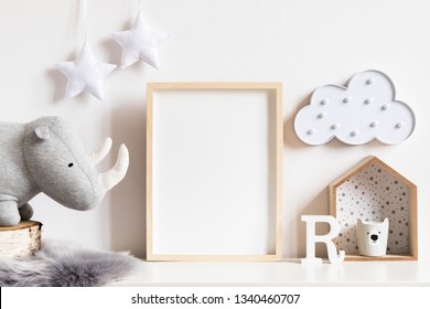 The modern scandinavian newborn baby room with mock up photo frame, wooden toy, plush rhino and clouds. Hanging cotton  white stars. Minimalistic and cozy interior with white walls.Real photo.Template