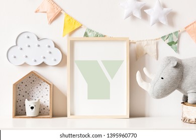 The modern scandinavian newborn baby room with mock up photo frame, wooden toy, plush rhino and clouds. Hanging cotton flags, white stars and cloud. Minimalistic and cozy decor of childroom.