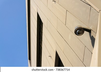 Modern security camera attached to wall with windows in background