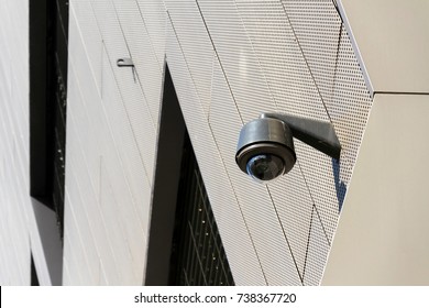 Modern security camera attached to wall with windows in background