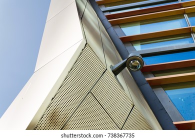 Modern security camera attached to wall with windows in background