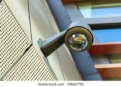 Modern security camera attached to wall with windows in background