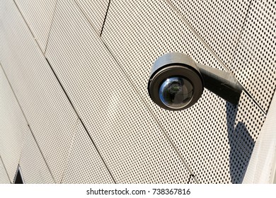 Modern security camera attached to wall with windows in background