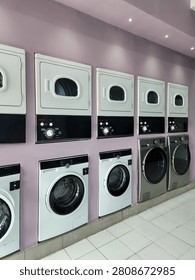 Modern self-service laundromat with rows of front-loading washing machines and tumble dryers in a clean, bright laundry facility