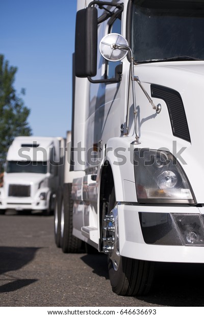 Modern semi trucks with a full-sized long flat\
bed trailer loaded with cargo are parked on truck stop in\
anticipation of the continuation of the begun route of delivery\
according to the\
schedule