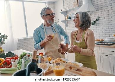 Modern senior couple in aprons preparing healthy dinner and smiling while spending time at home - Powered by Shutterstock