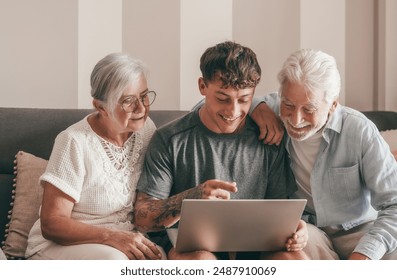 Modern senior couple learning computer technology from experienced young grandson, handsome smiling boy teaching to his grandparents how to use computer, make online shopping, book travel and vacation - Powered by Shutterstock