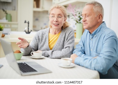 Modern senior couple sitting by table in front of laptop and discussing webcast by cup of tea - Powered by Shutterstock