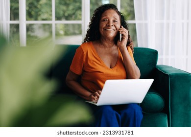 Modern senior woman working from the comfort of her home office, making business calls and feeling accomplished as she balances life and work. Mature business woman sitting on her couch with a laptop. - Powered by Shutterstock