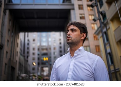 Modern serious businessman near building. Confident young man in white shirt looking to the side while standing outdoors with cityscape in background - Shutterstock ID 2059481528