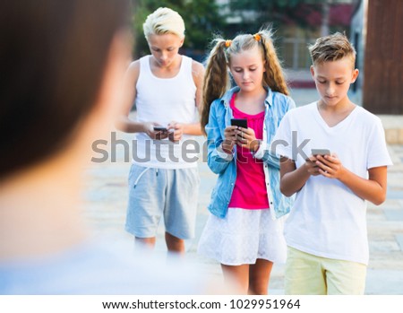 Modern serious kids spending time together outdoors using mobile gadgets