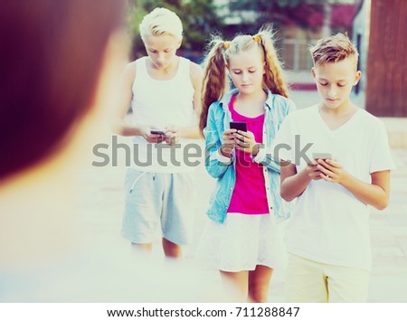 Modern serious kids spending time together outdoors using mobile gadgets