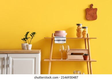 Modern shelving unit with dishware and houseplants near yellow wall in kitchen