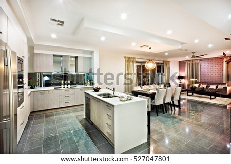 Modern and shiny kitchen with dining and living area, including a counter top and kitchenware on the reflective tiles, there are lights flashing at night