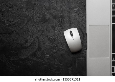 Modern silver laptop with a mouse on dark background. Top view and copy space.