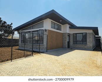 A modern single-story house features an angular roof and brick facade, embodying contemporary architectural design. The clear blue sky enhances the residential setting.