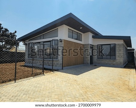 A modern single-story house features an angular roof and brick facade, embodying contemporary architectural design. The clear blue sky enhances the residential setting.