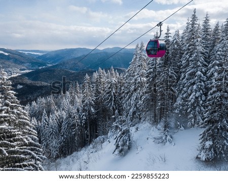 Modern ski lift gondola against snowcovered fir forest and mountains