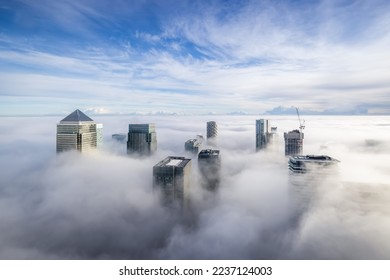 The modern skyline of Canary Wharf, London, during a foggy day with the tops of the skyscrapers looking out of the clouds - Shutterstock ID 2237124003