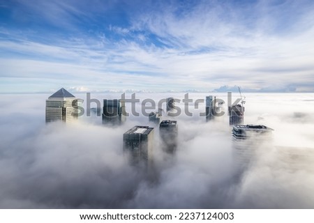The modern skyline of Canary Wharf, London, during a foggy day with the tops of the skyscrapers looking out of the clouds