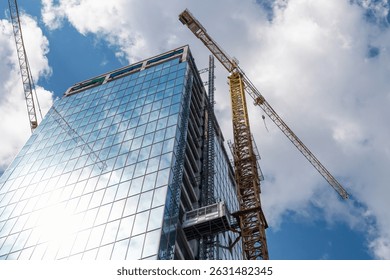 Modern skyscraper construction with tower cranes against blue sky.