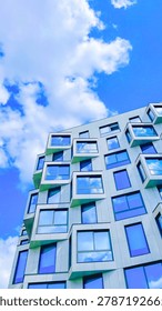 Modern skyscraper facade featuring unique geometric protruding windows captured from a low angle against a bright blue cloudy sky background