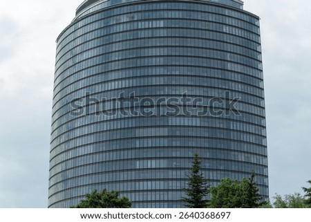 Modern skyscraper with glass facade in urban setting. The interplay of nature and architecture in a bustling metropolis. Reflections of ambition and innovation in a corporate landscape.