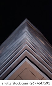  Modern skyscraper's sharp corner is captured against the night sky, its facade and geometric lines highlighting a sleek, futuristic design.